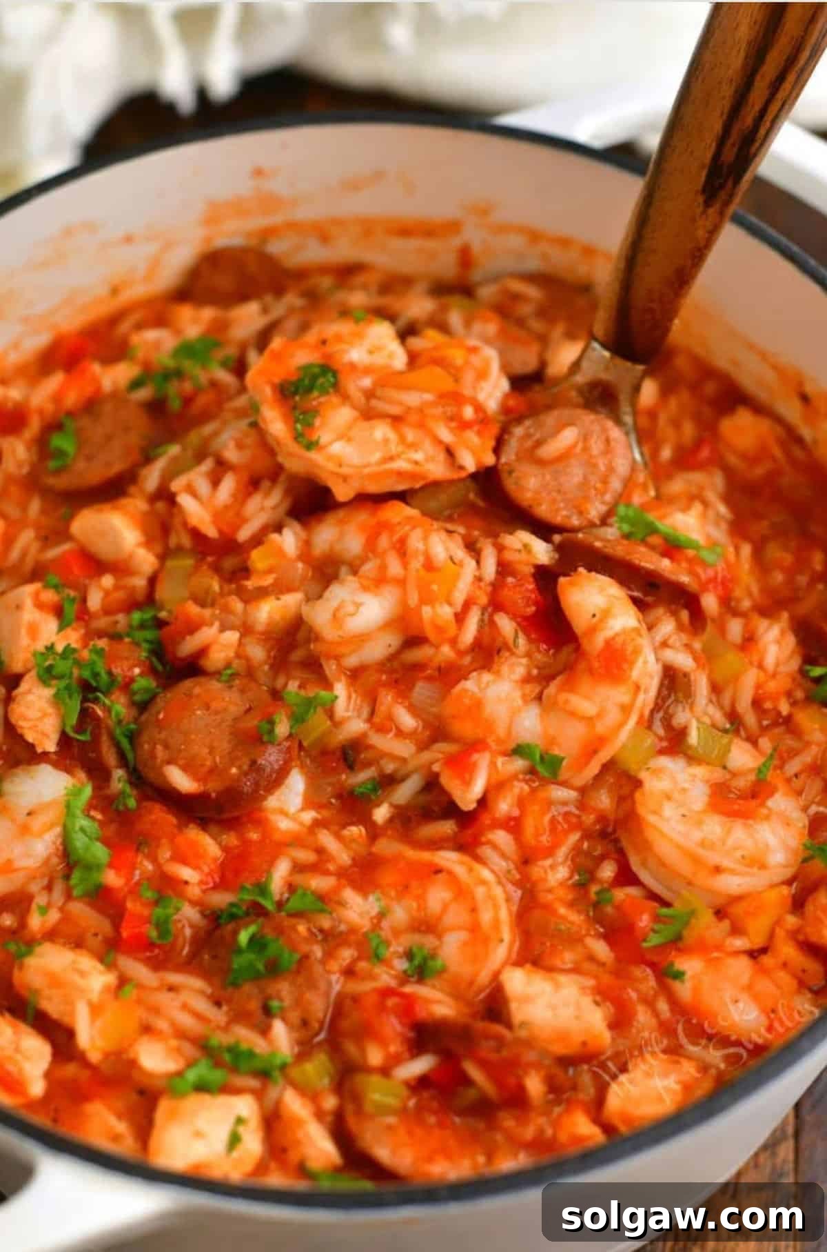 A ladle scooping a generous portion of flavorful Jambalaya out of a large cooking pot, showcasing the hearty mixture of rice, meats, and vegetables.