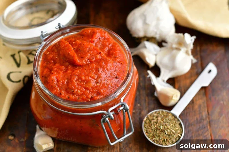 pizza sauce without tomato paste in small glass jar next to fresh garlic cloves and dried oregano