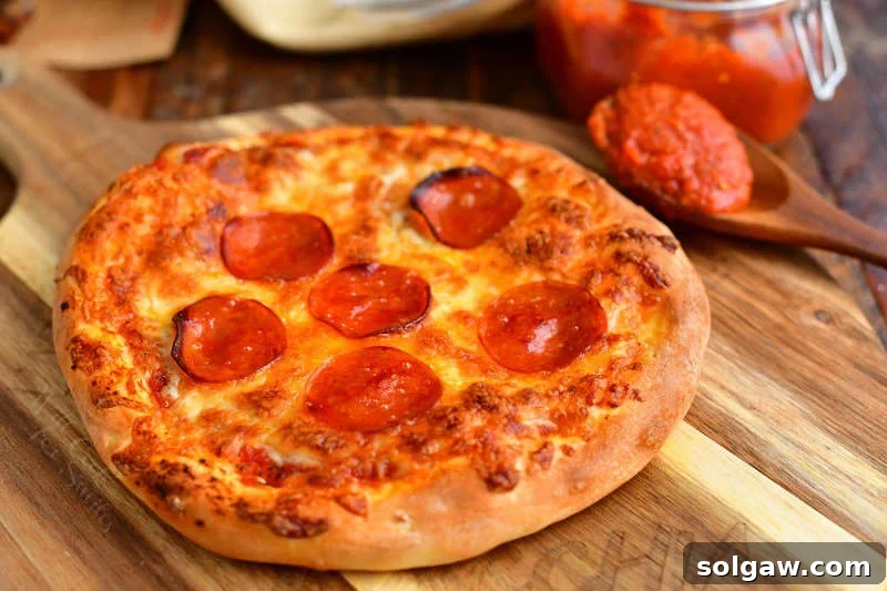 pizza sauce with tomato paste on wooden spoon next to pepperoni pizza