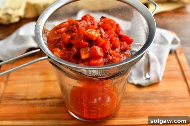 straining diced tomatoes through fine mesh strainer into measuring cup