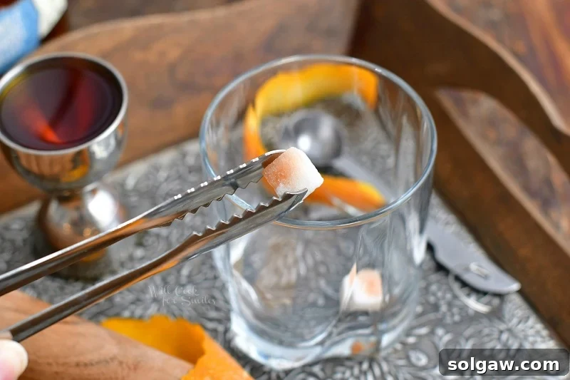 holding sugar cube in metal tongs over a cocktail glass