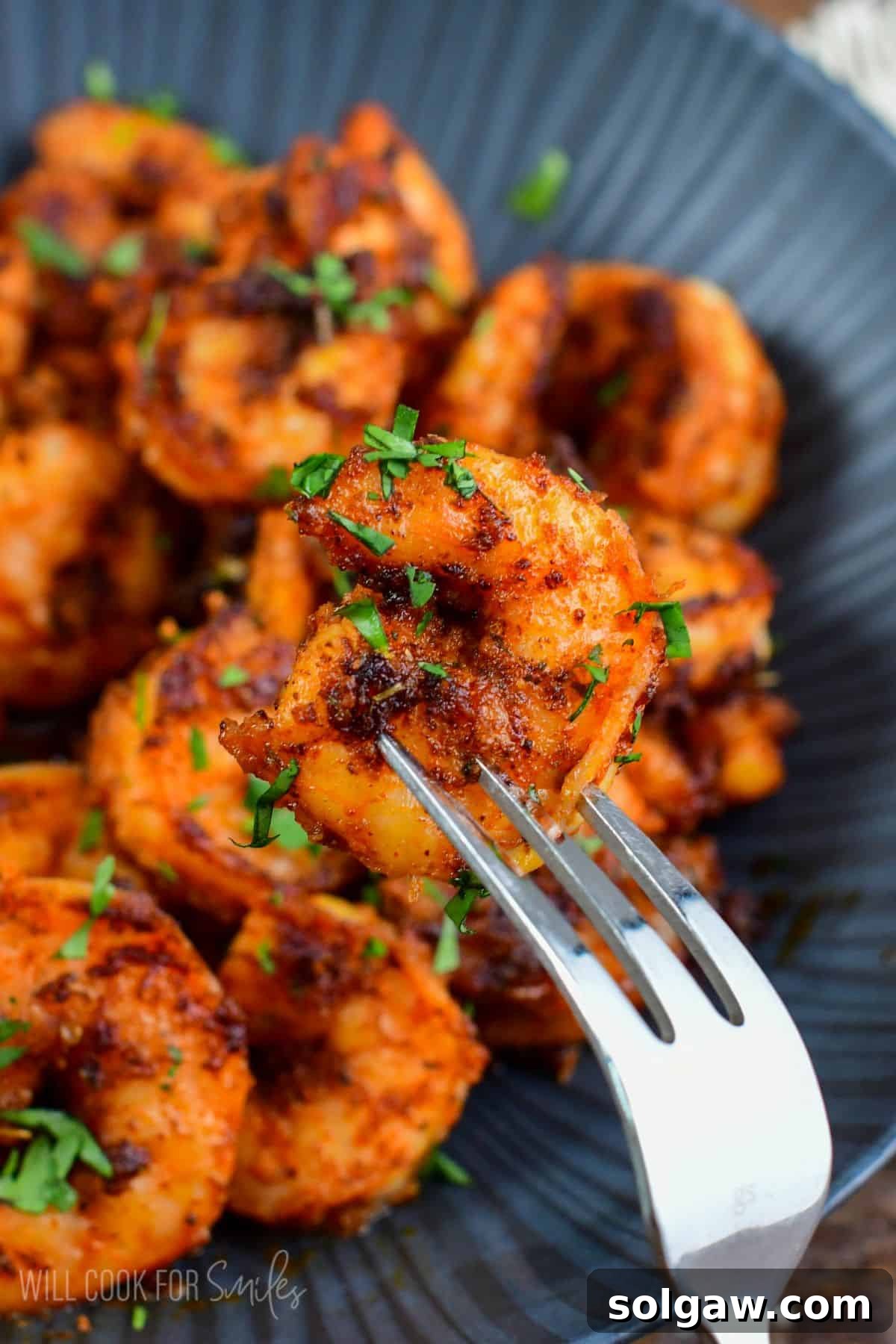 Smoky Cajun Shrimp 5 holding one blackened shrimp on a fork in front on a bowl.