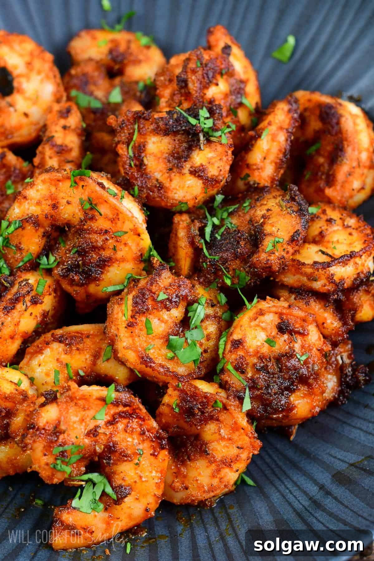 A pound of cooked blackened shrimp in a black bowl with parsley garnish.