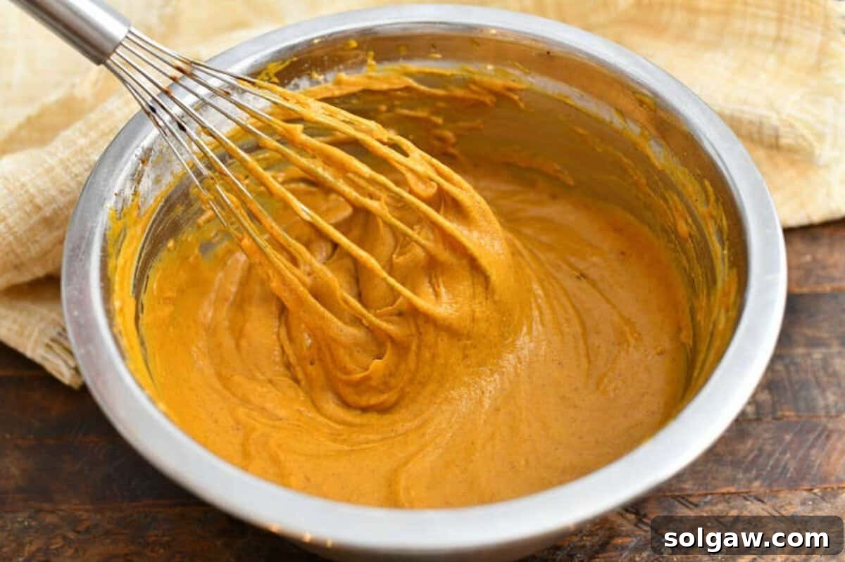 Homemade Pumpkin Spice Latte Donuts 4 Whisking pumpkin batter in a bowl, showing the smooth, orange consistency for baked donuts.