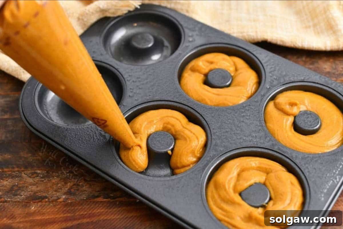 Homemade Pumpkin Spice Latte Donuts 5 Using a pastry bag to neatly fill the wells of a donut pan with pumpkin spice latte batter.