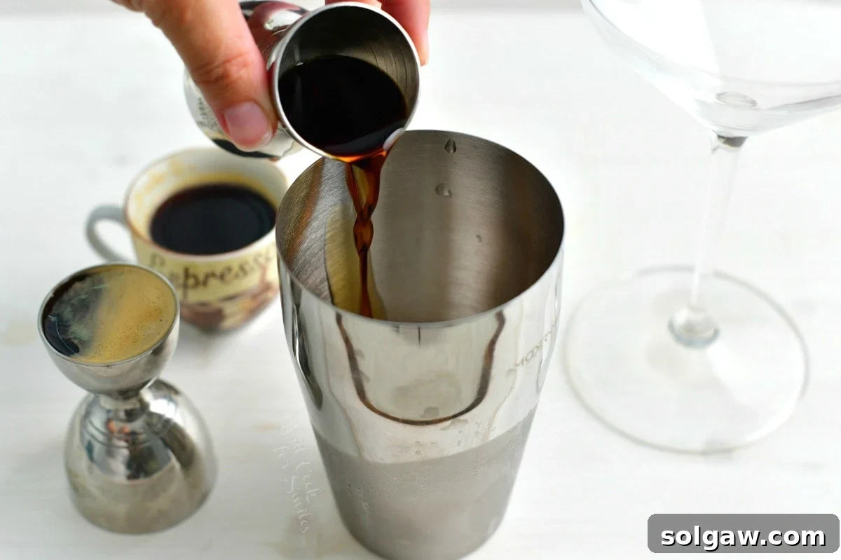 A stream of dark brown coffee liqueur (Kahlua) being poured into a cocktail shaker alongside other ingredients.