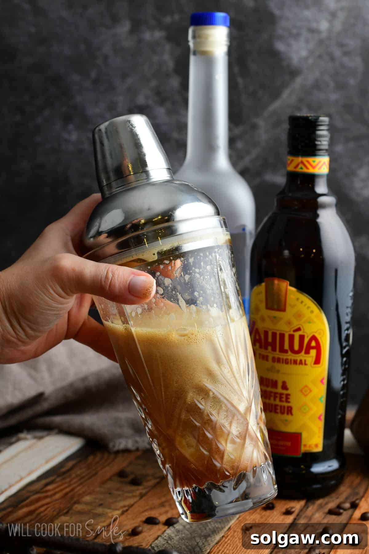 A bartender holding a condensation-covered cocktail shaker, freshly shaken, with espresso martini inside, ready to be poured.