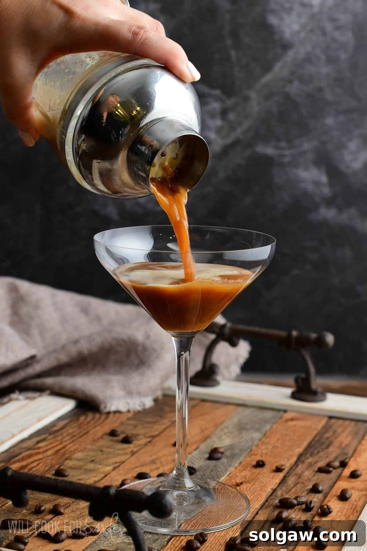 Close-up of an espresso martini being poured from a cocktail shaker through a strainer into a chilled martini glass, showcasing the frothy top layer.