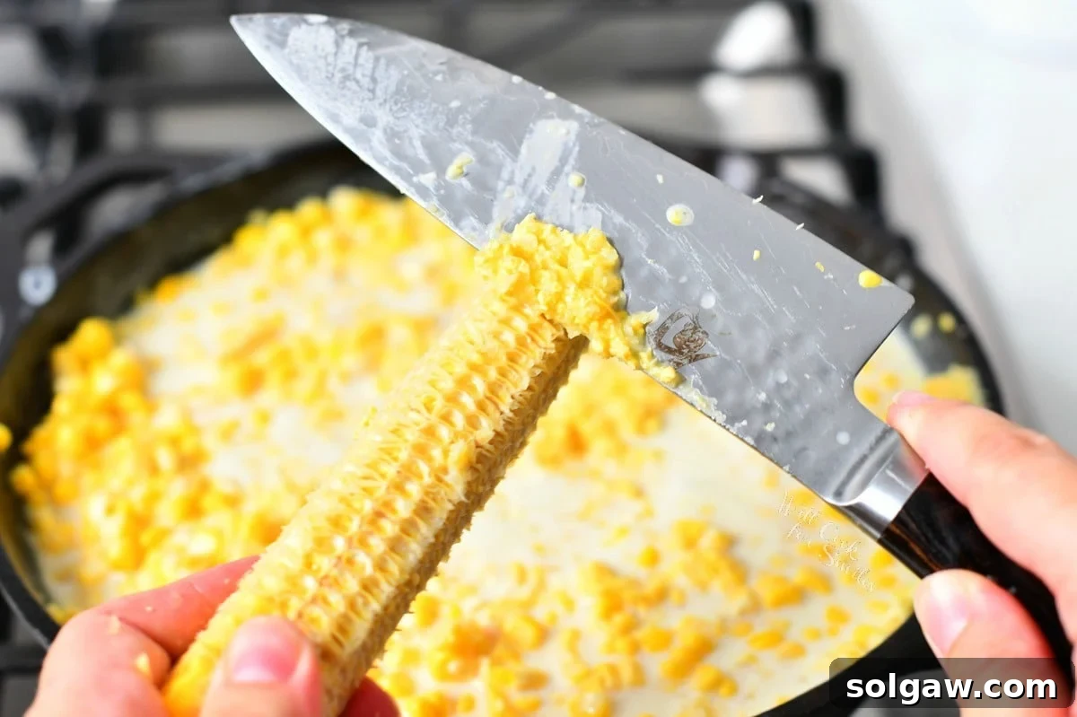 using the back of a chef's knife to remove fresh corn from a cob
