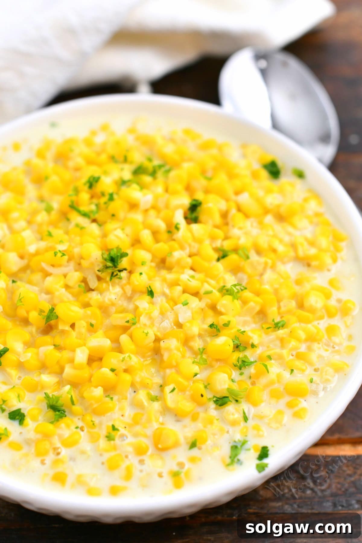 yellow corn vegetable side dish in a white bowl garnished with fresh parsley