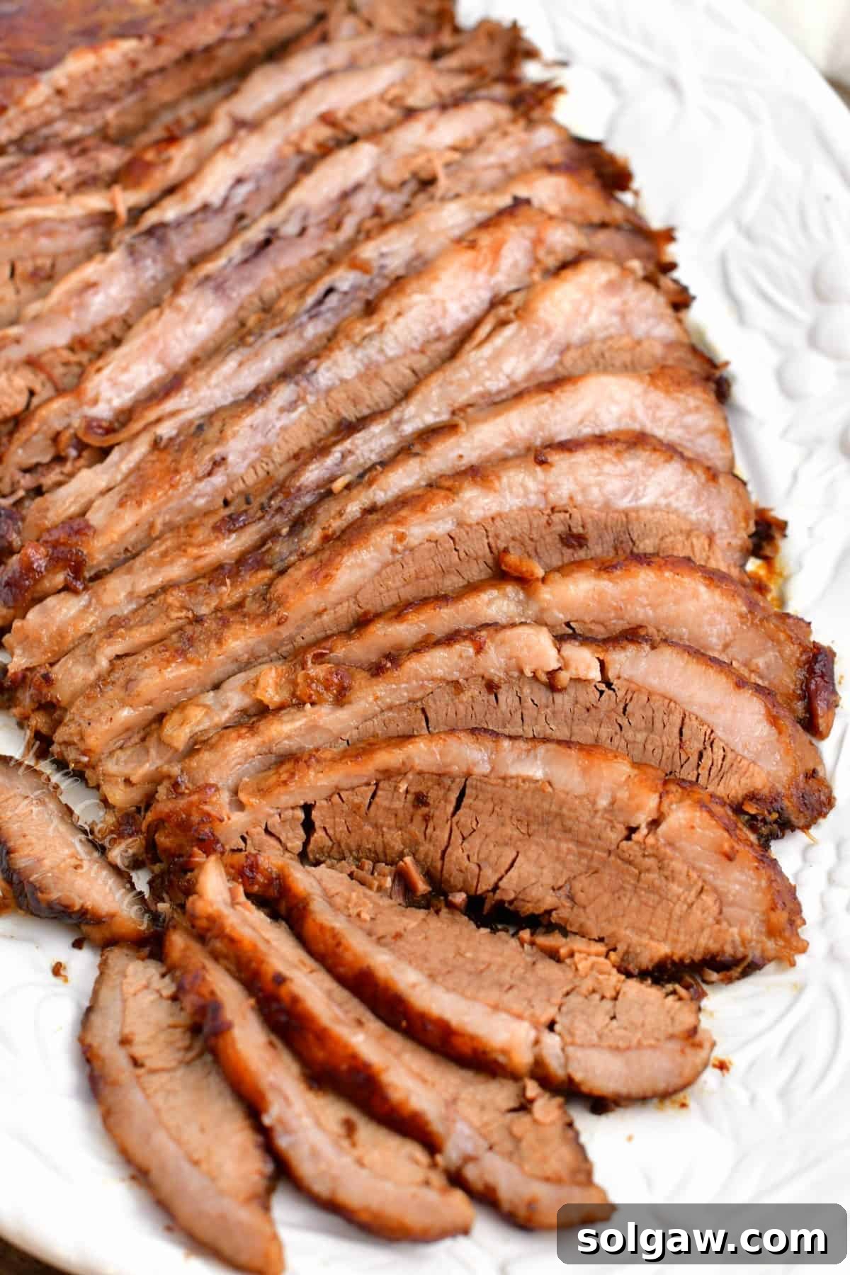 Close-up of thin slices of perfectly oven-baked beef brisket on a pristine white serving platter