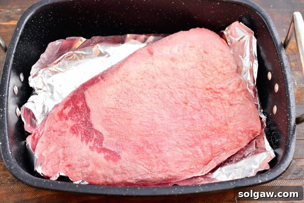 Overhead view of an uncooked brisket, meticulously placed in a large, foil-lined roasting pan, ready for seasoning and refrigeration.