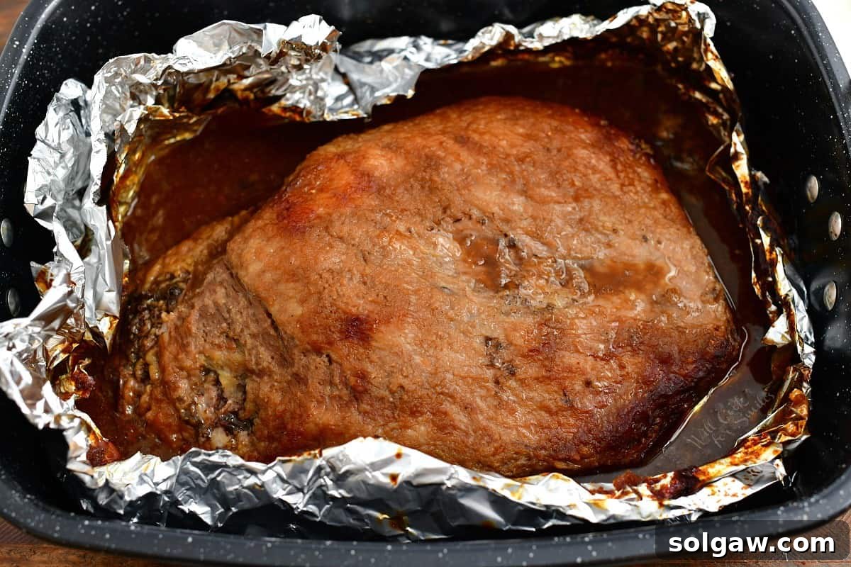 Overhead perspective of a large beef brisket enveloped in aluminum foil, nestled in a roasting pan within the oven, undergoing its slow cooking process.