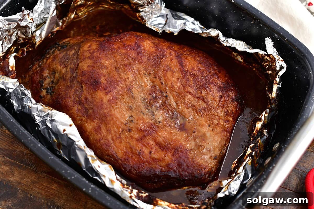 An overhead shot revealing a beautifully cooked beef brisket, removed from its foil covering, resting in a roasting pan after its final uncovered cooking stage in the oven.