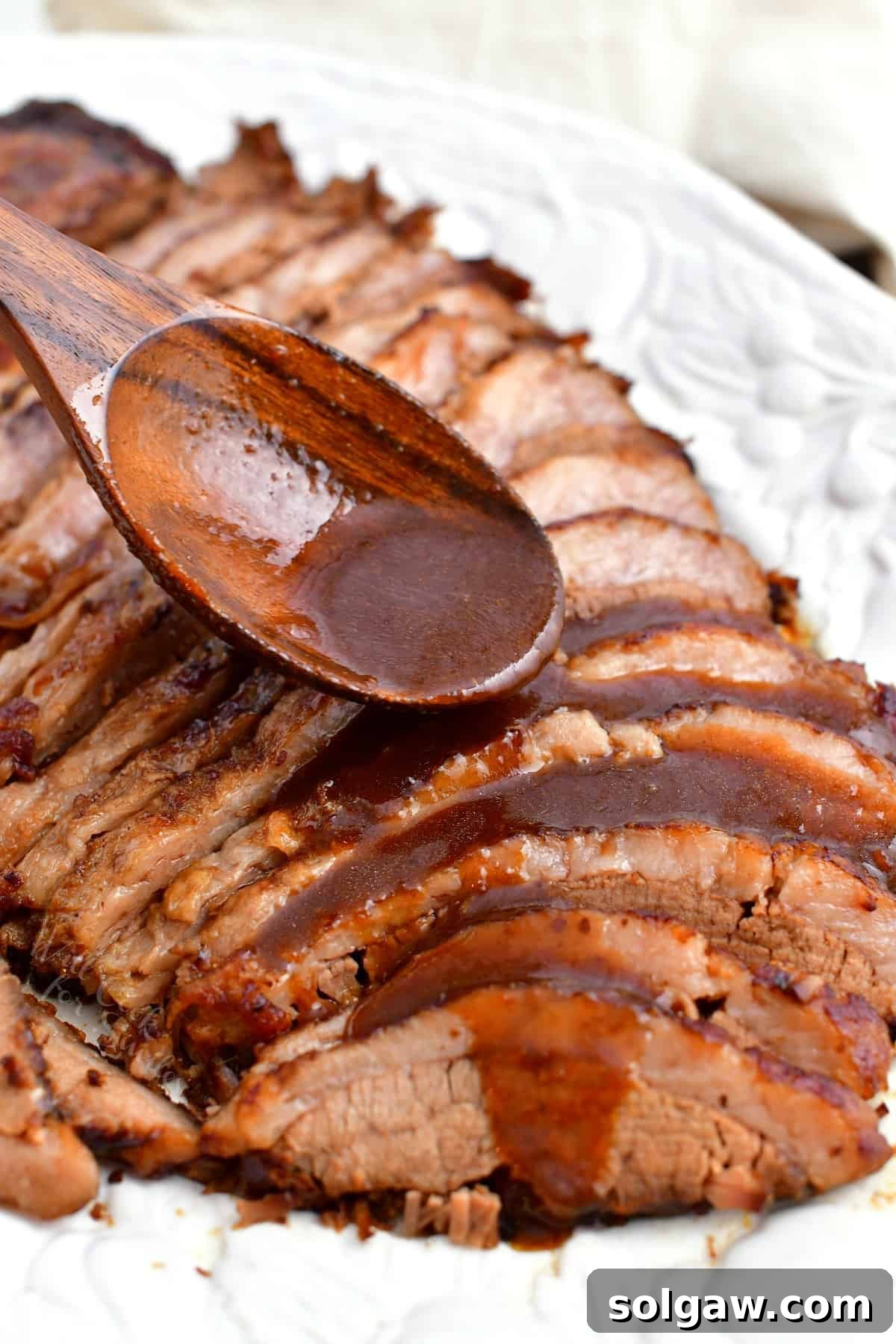 A hand ladling rich balsamic sauce over tender, thinly sliced beef brisket, showcasing the perfect presentation for a gourmet meal.