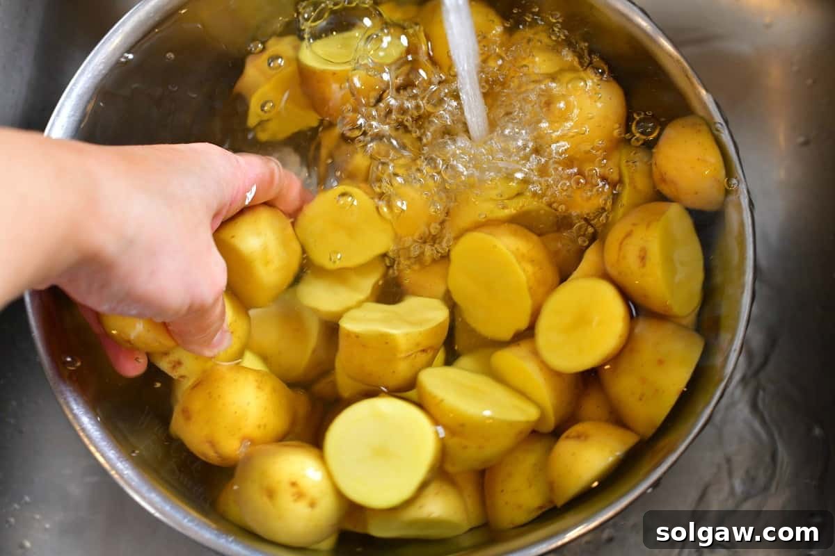 A bowl of sliced Yukon Gold potatoes being rinsed under cold tap water to remove excess starch.