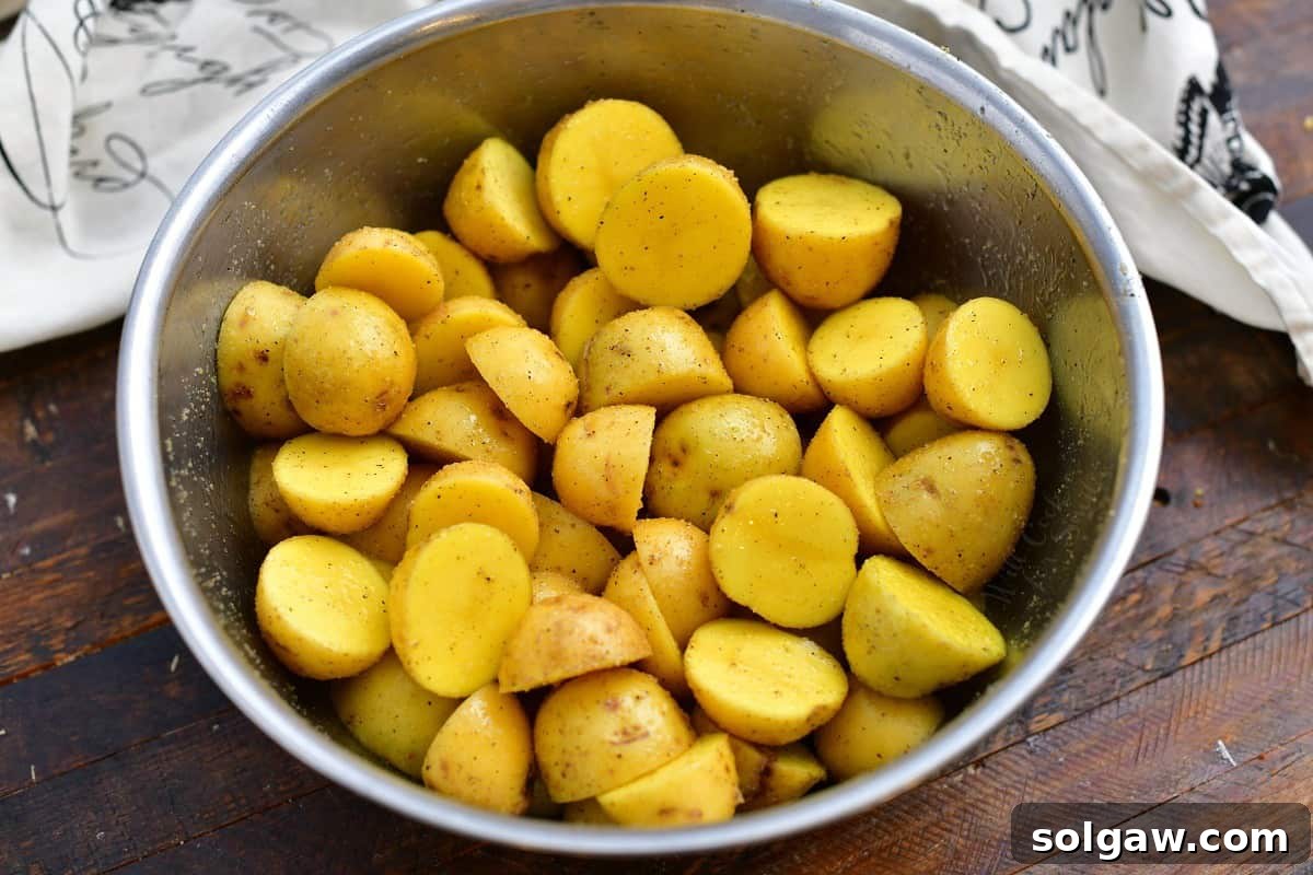 A mixing bowl filled with raw Yukon Gold potatoes, uniformly sliced in half, ready for seasoning.