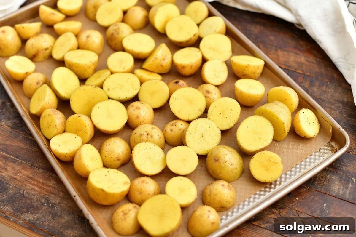 Seasoned yellow potatoes arranged in a single layer on a parchment-lined baking sheet, prepared for oven roasting.