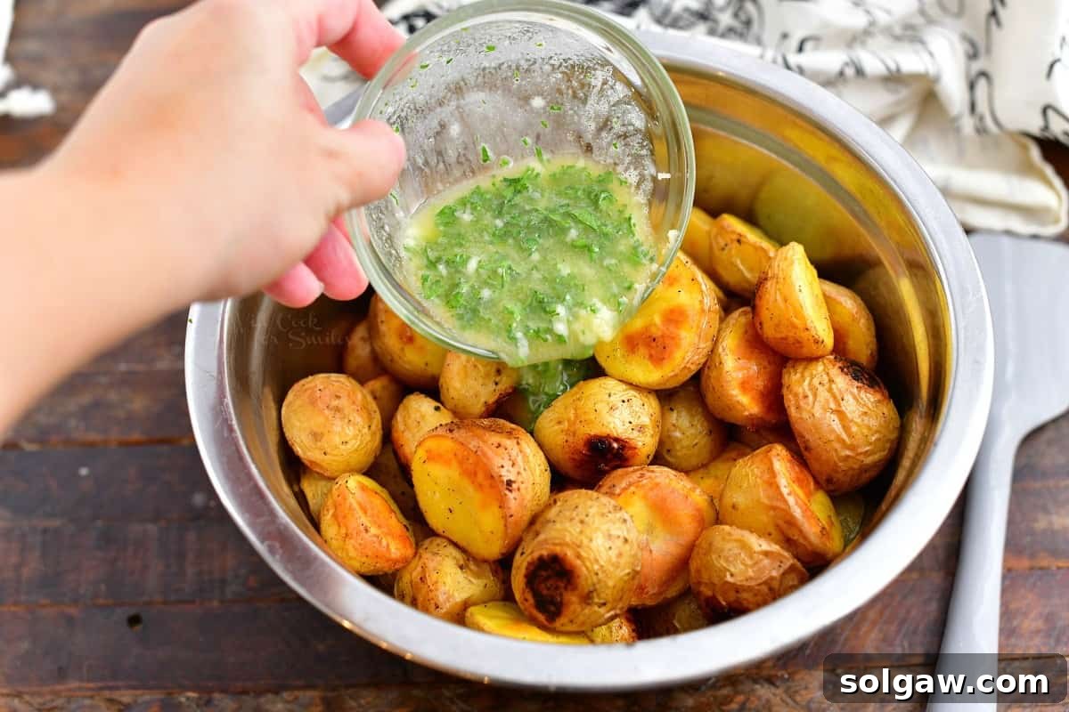 Savory herb butter being poured generously over a bowl of freshly roasted potatoes, enhancing their flavor and shine.
