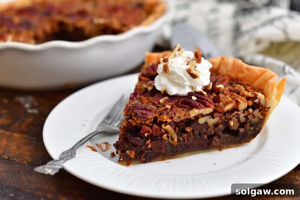 A close-up side view of a slice of chocolate pecan pie topped with whipped cream on a white plate.