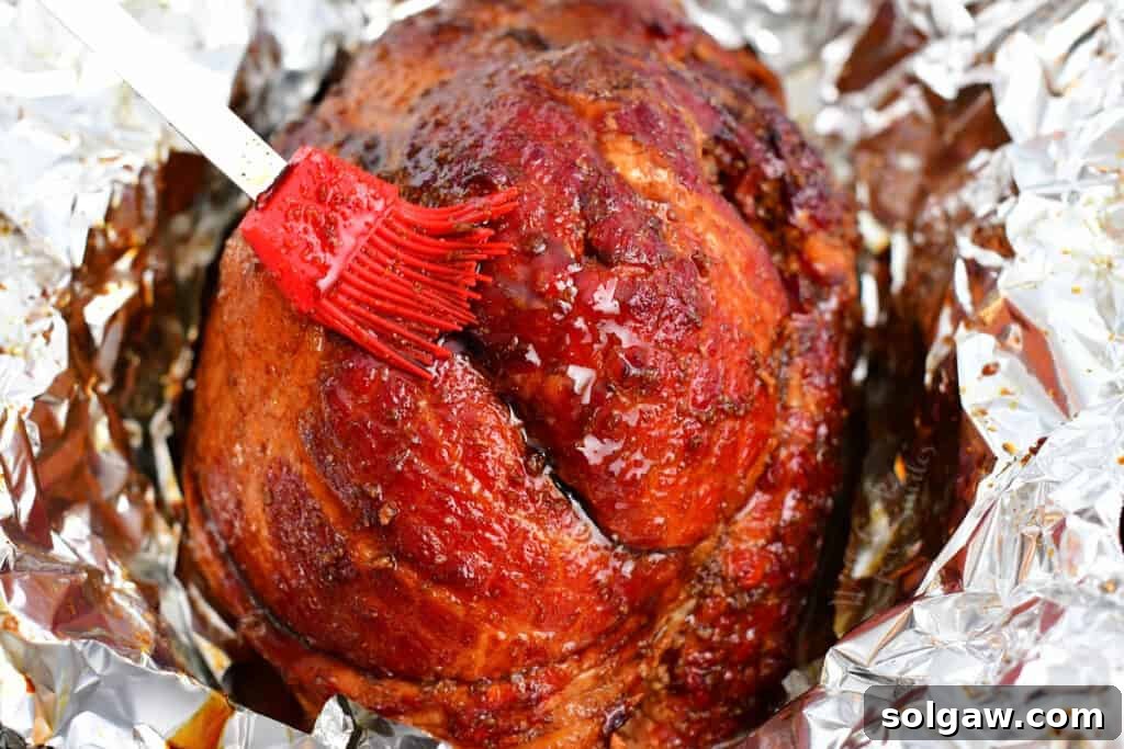 Signature Bourbon Glazed Ham 6 A baking ham on a tray, being generously brushed with more bourbon glaze for a perfect finish.