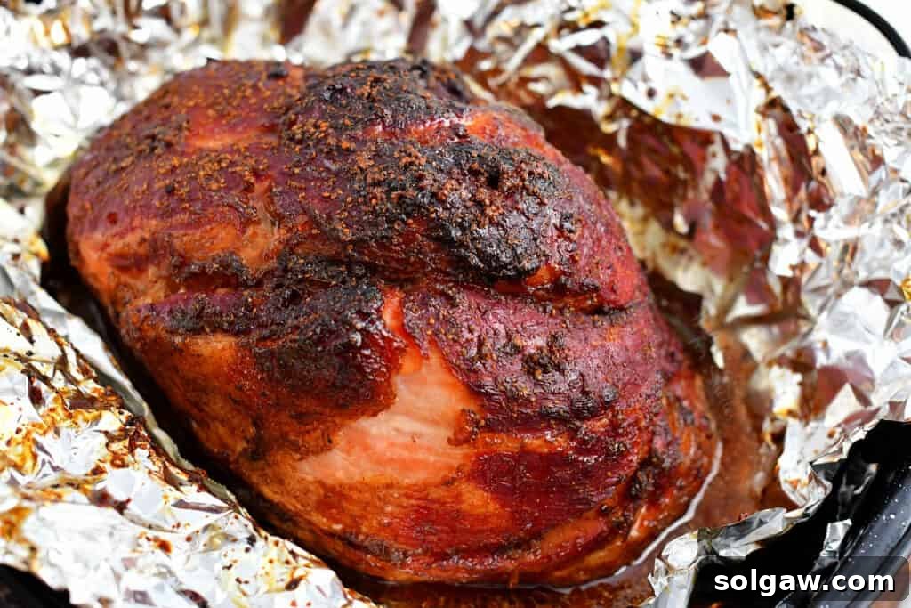 Signature Bourbon Glazed Ham 7 A perfectly baked bourbon glazed ham rests on a foil-lined baking pan, its caramelized crust gleaming.