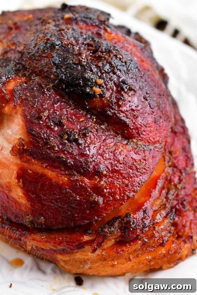 Signature Bourbon Glazed Ham 8 A close-up view of a crispy, golden-brown baked ham, glistening with bourbon glaze, on a white serving platter.