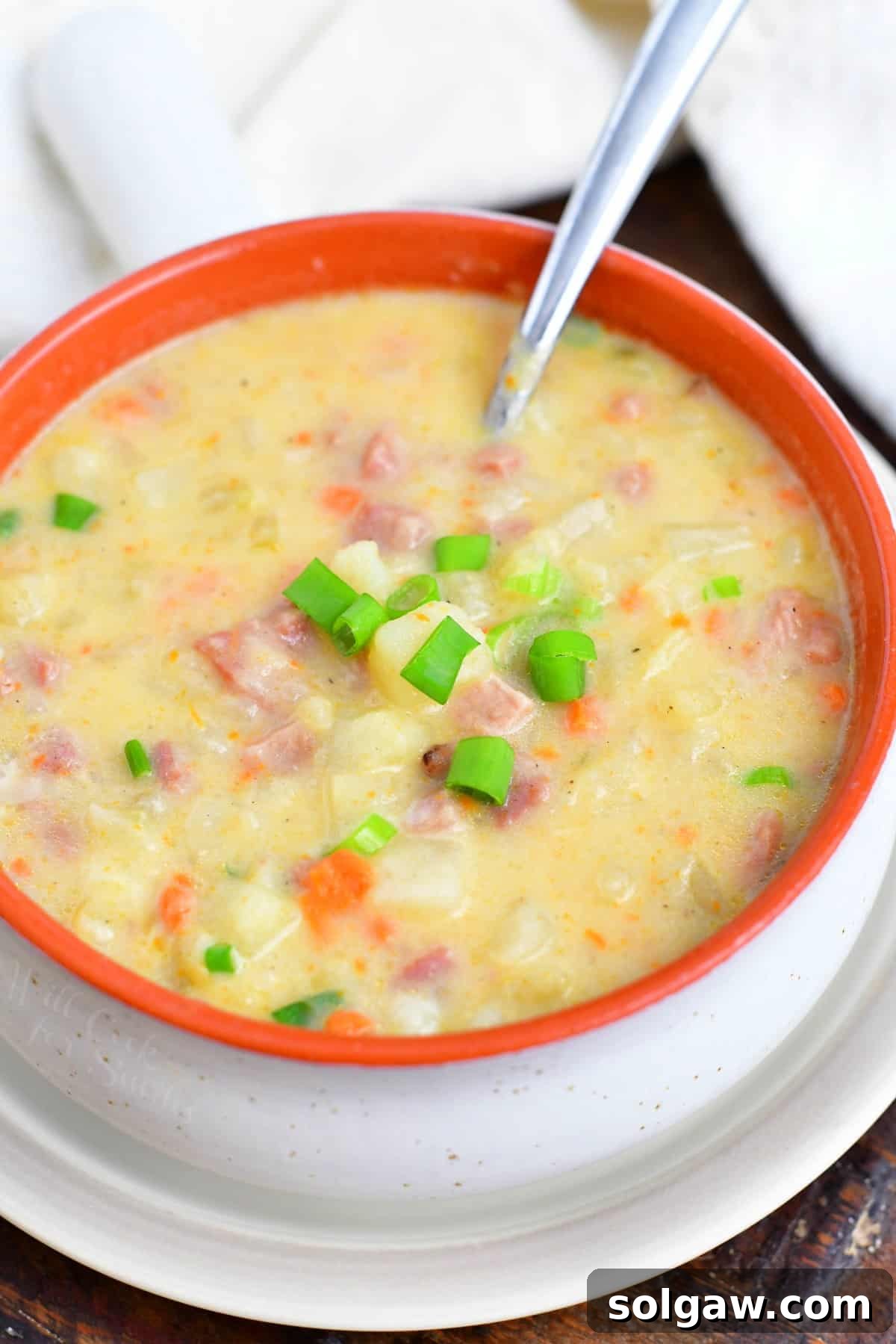 A ladle in a bowl of creamy ham and potato soup with fresh garnishes.