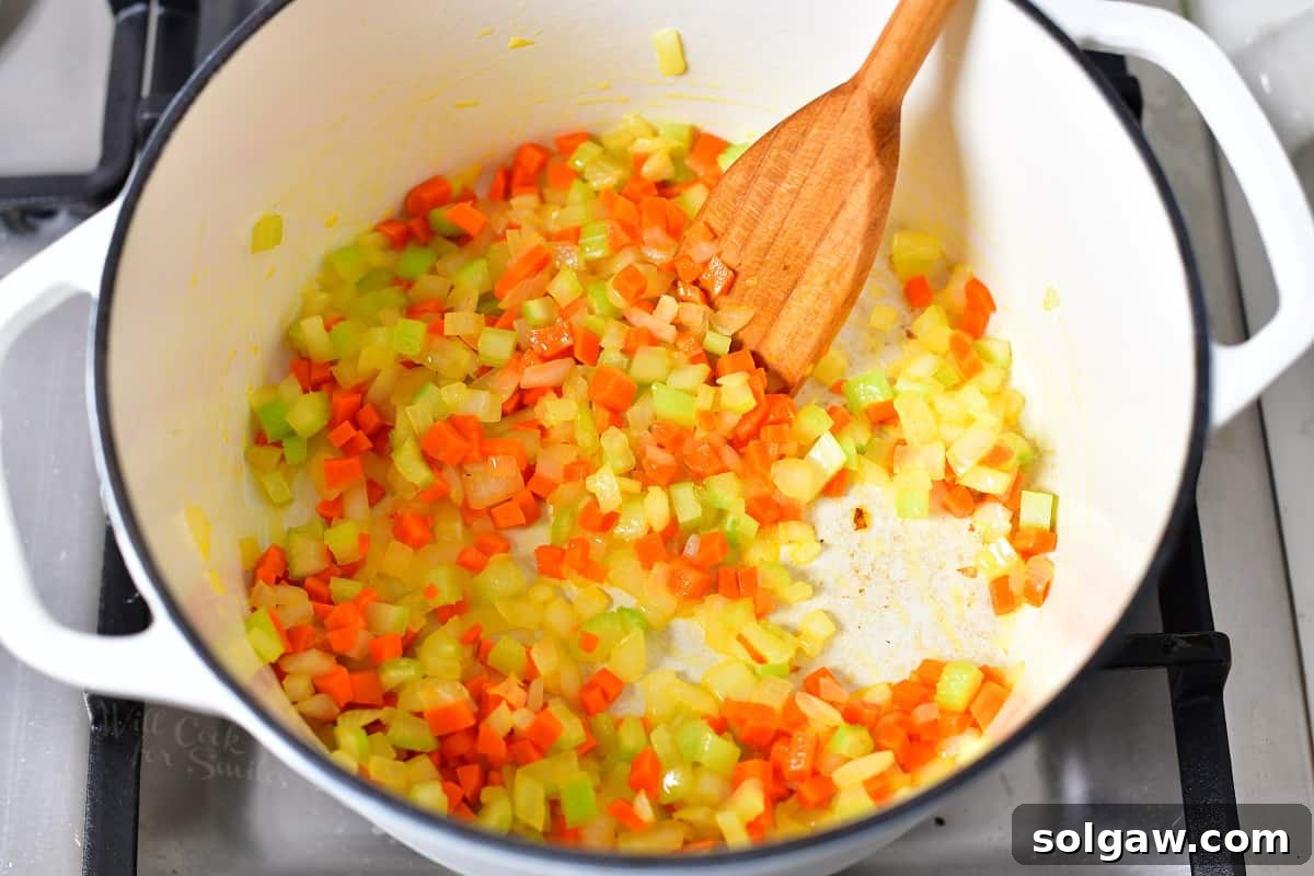 Overhead view of diced onions, carrots, and celery being sautéed in a large pot with oil.