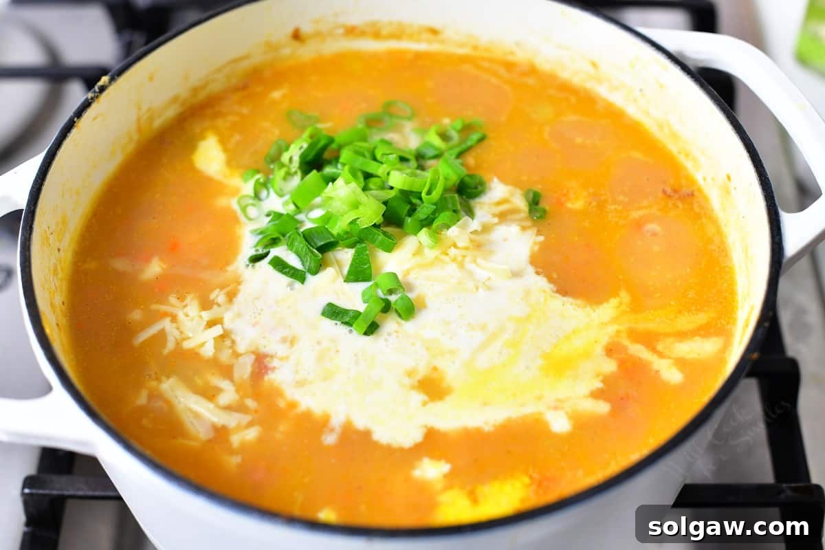 Fresh scallions and heavy cream being added simultaneously to a pot of ham and potato soup.