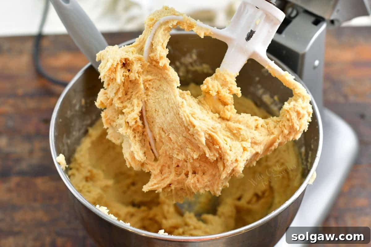 Soft, sticky eggnog cookie dough being scraped from an electric beater into a bowl.