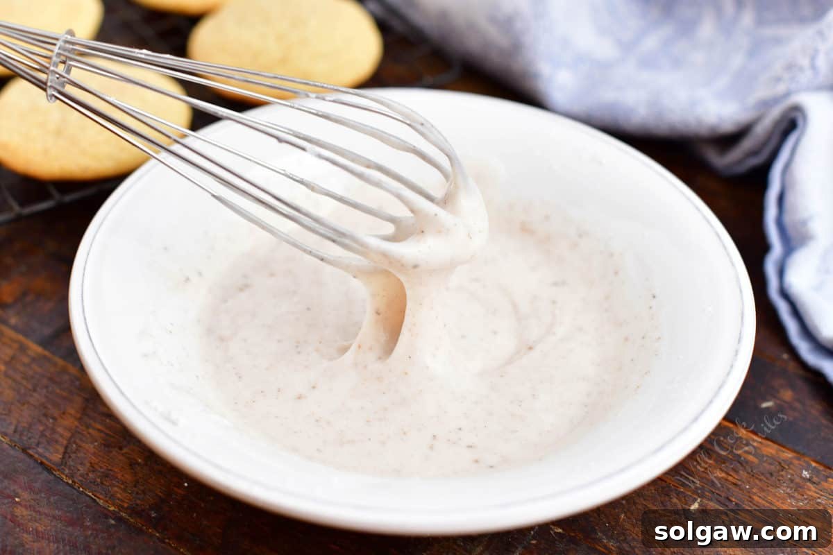 Smooth, white eggnog icing being whisked in a shallow white bowl.