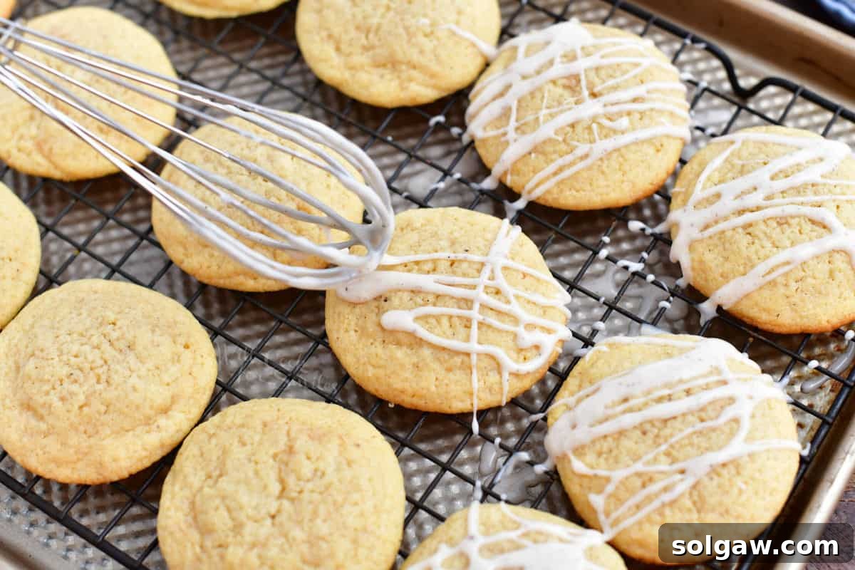 Creamy eggnog icing drizzled elegantly from a whisk onto freshly baked eggnog cookies.