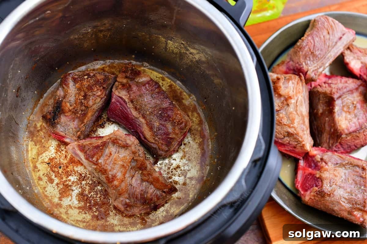 Pieces of beef short rib searing in the Instant Pot, developing a rich brown crust for maximum flavor.