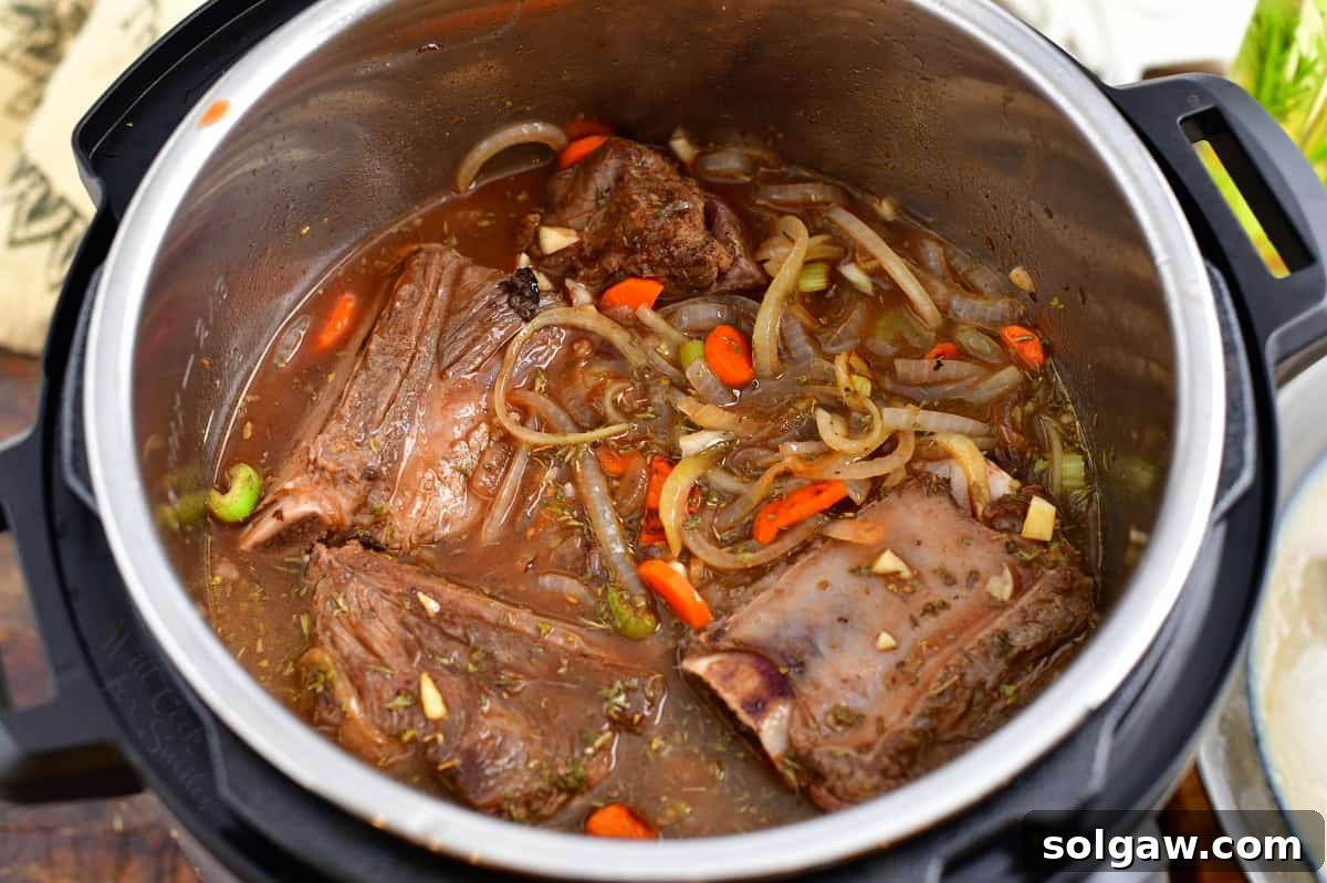 Fully cooked beef short ribs and tender vegetables nestled in the rich sauce within the Instant Pot, ready for final sauce thickening.