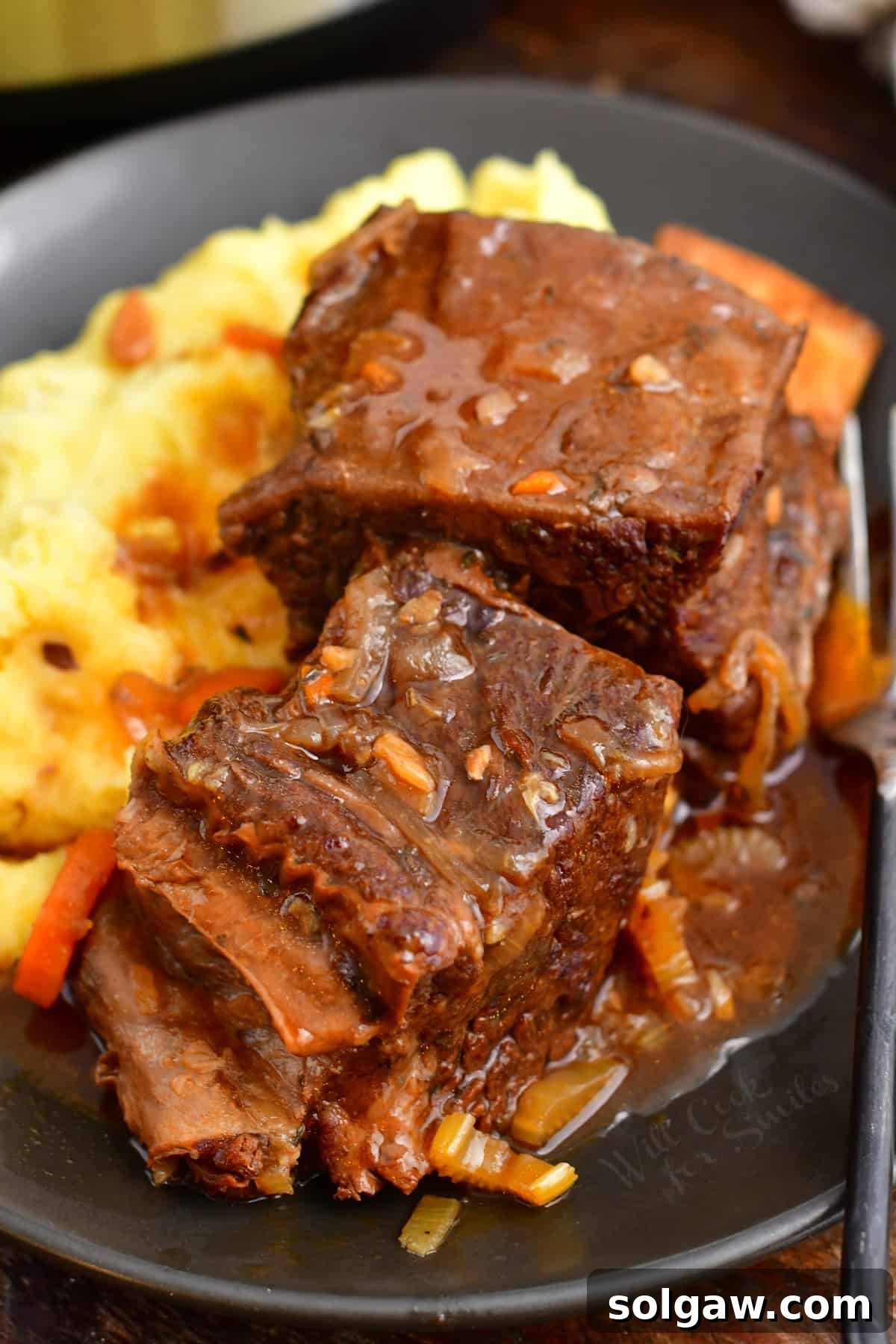 Two pieces of perfectly cooked Instant Pot short ribs nestled on a bed of mashed potatoes, with fresh parsley garnish.