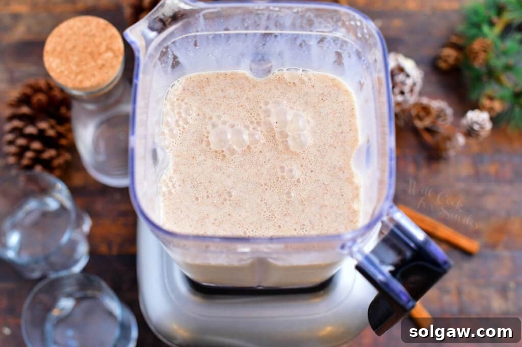 An overhead photo highlighting the key creamy ingredients in a blender, including coconut milk, condensed milk, and a sprinkle of cinnamon and nutmeg, ready to be blended for Coquito.