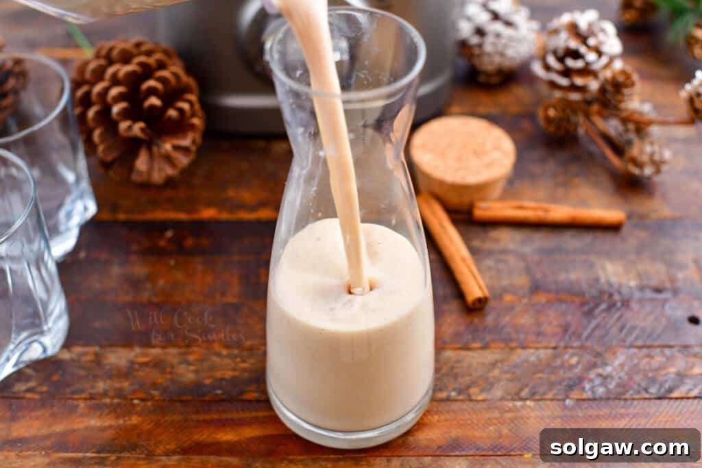 A hand is shown carefully filling a clear glass pitcher with the rich and creamy Puerto Rican Christmas drink, Coquito, after blending.
