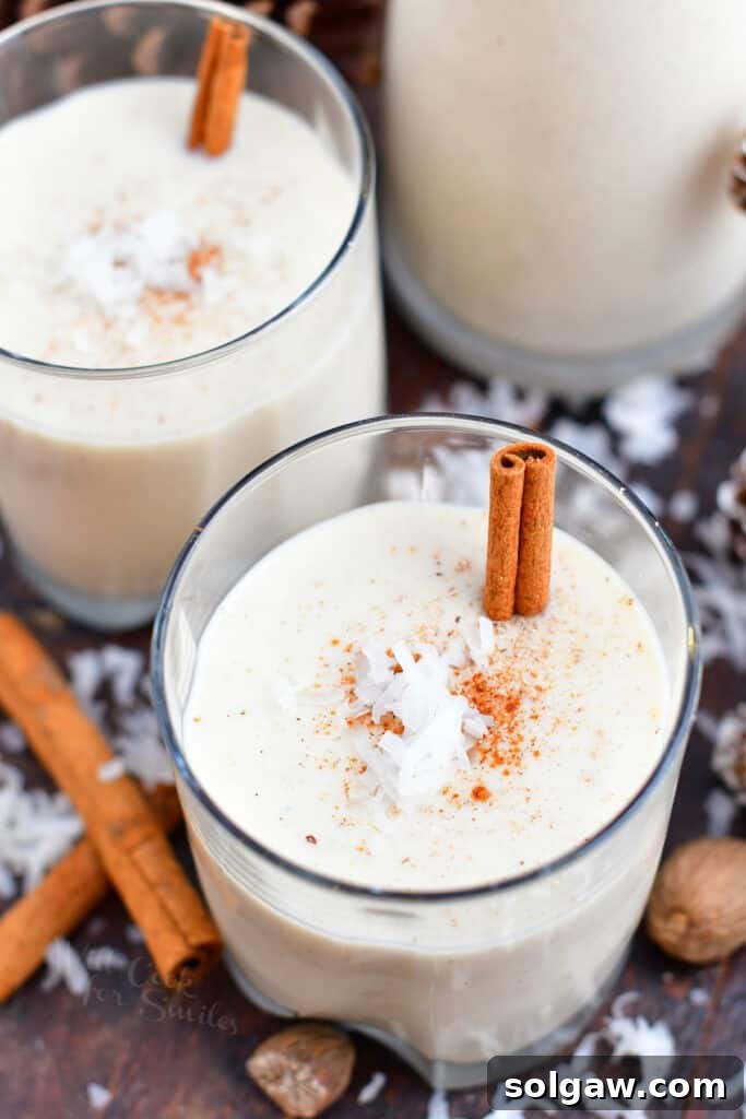 A stunning close-up of a Puerto Rican Christmas drink, Coquito, served in two glasses, garnished with fragrant cinnamon sticks and delicate coconut flakes, capturing the essence of the holidays.