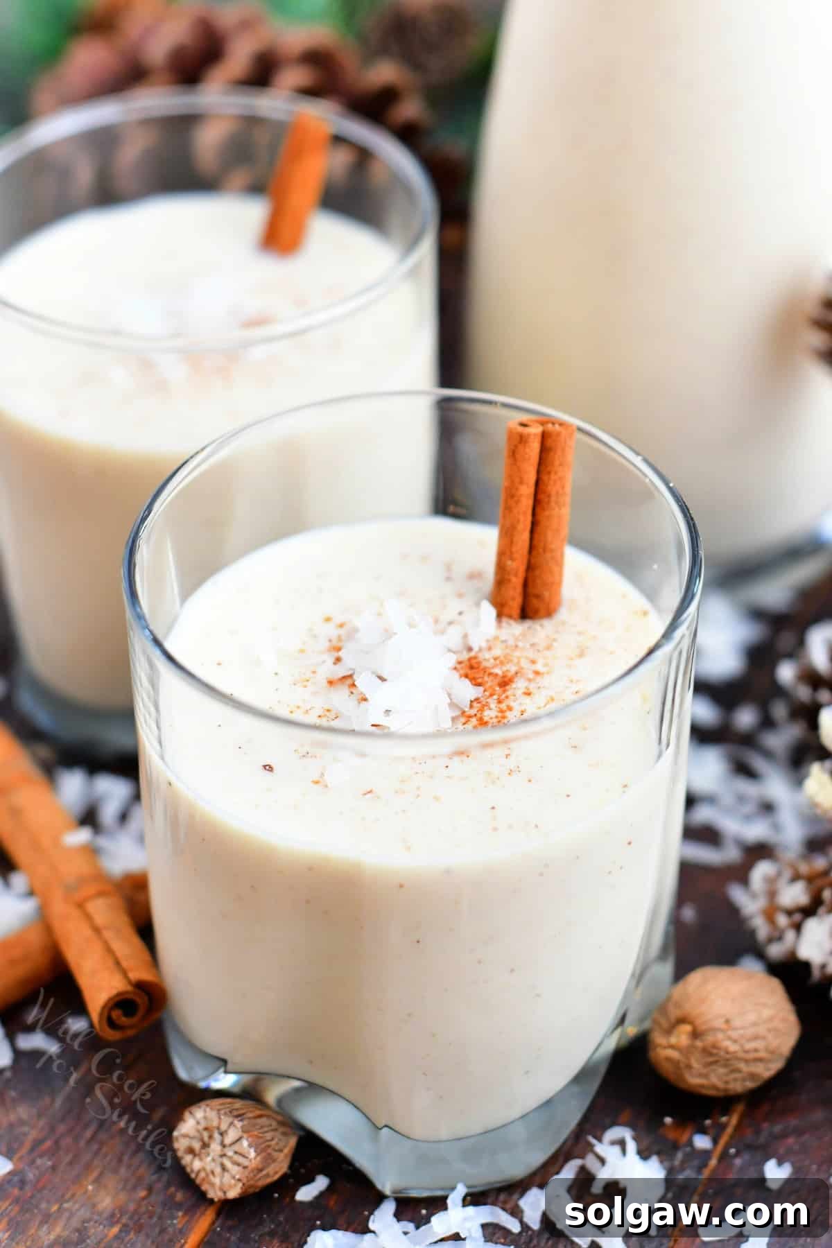 Two glasses of Coquito, elegantly garnished with cinnamon sticks and coconut flakes, ready to be enjoyed.