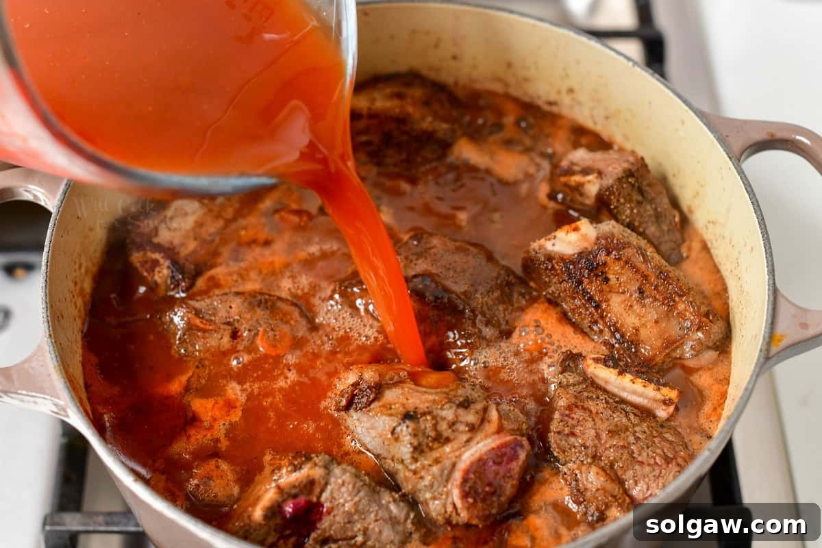 pouring stock into a large pot with braised beef ribs