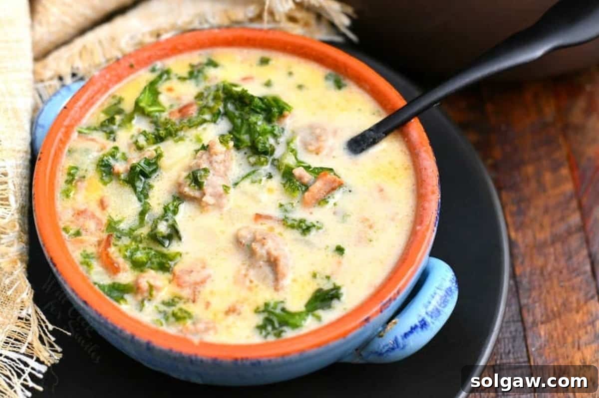 A beautifully presented bowl of Zuppa Toscana soup on a black plate with a spoon to the right.