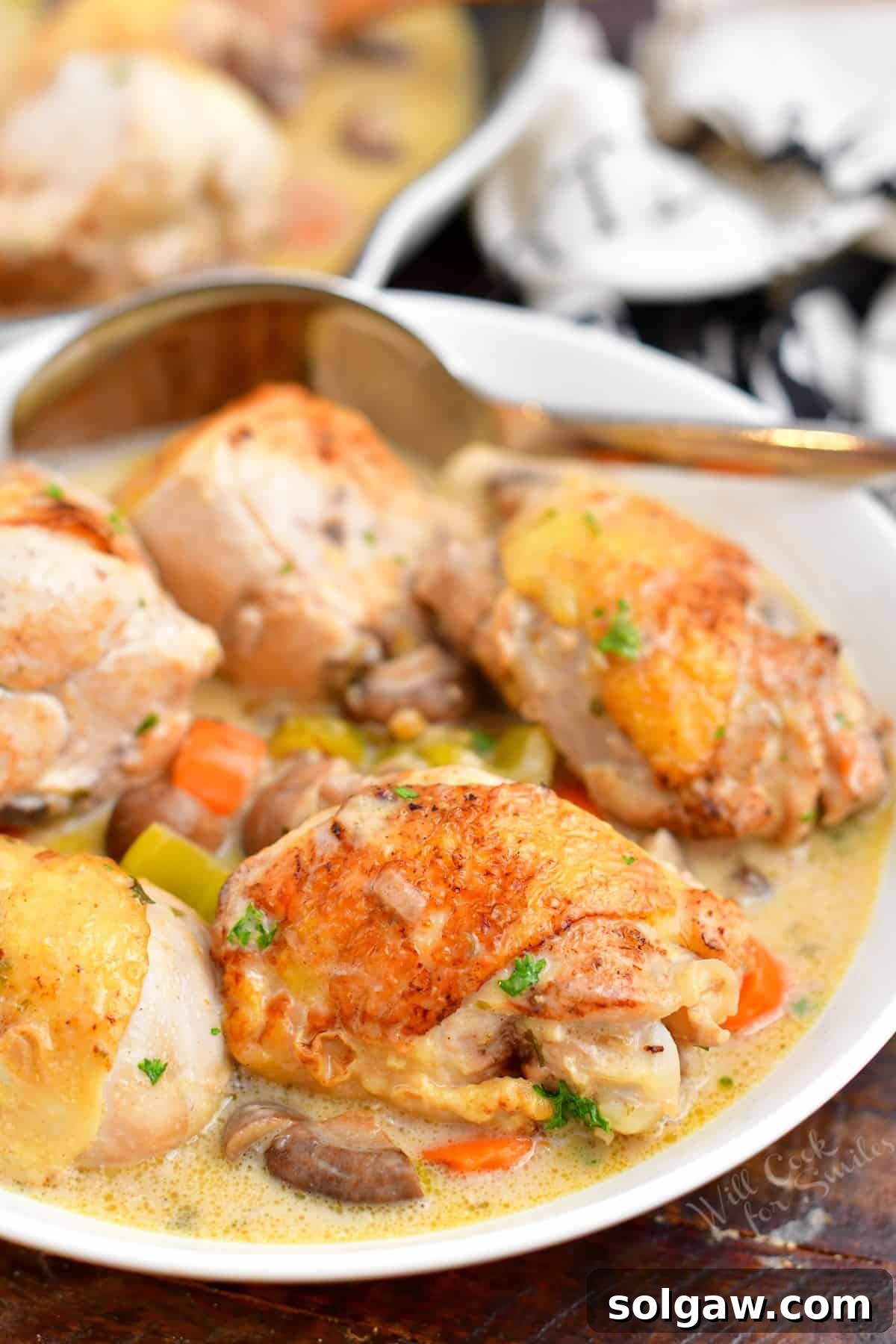 A beautifully cooked meal of chicken thighs and drumsticks nestled with mixed vegetables in a rich, creamy white sauce, ready to be served.