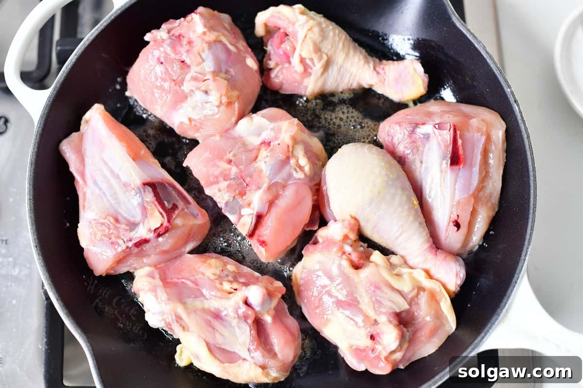 Raw, bone-in chicken pieces, lightly seasoned, sizzling in a frying pan with melted butter, beginning to brown.