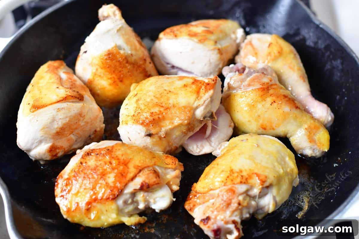 Bone-in chicken pieces browning to a golden color in a cast iron skillet, creating rich fond.