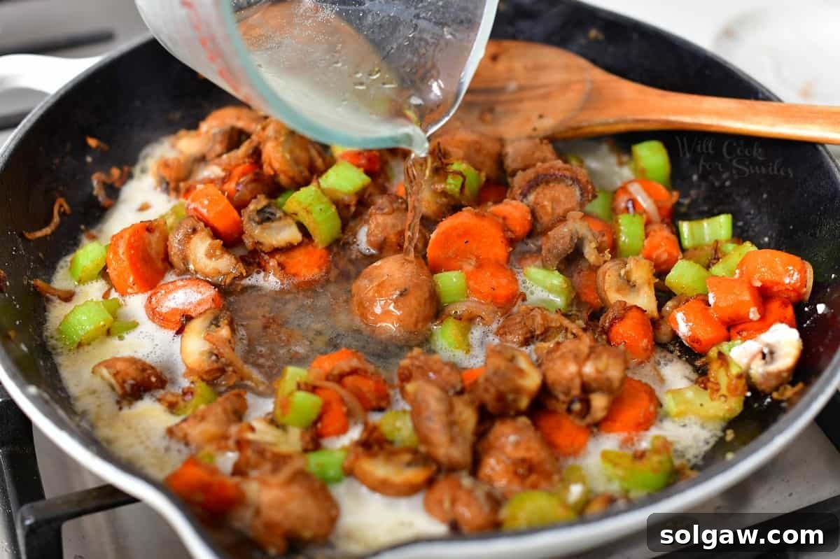Pouring dry white wine into a skillet of cooked vegetables and roux, deglazing the pan for Chicken Fricassee.