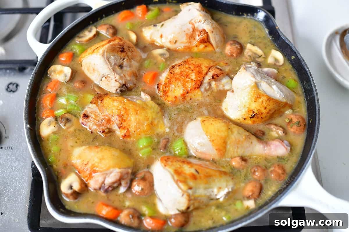 Chicken Fricassee simmering gently in a white enameled skillet on the stovetop, infusing flavors.