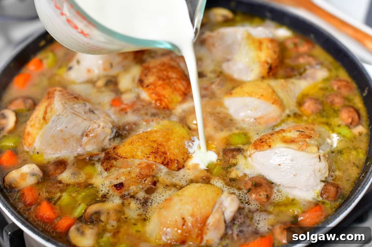 Pouring rich heavy cream into a skillet of cooked chicken stew, adding the final touch to the fricassee.