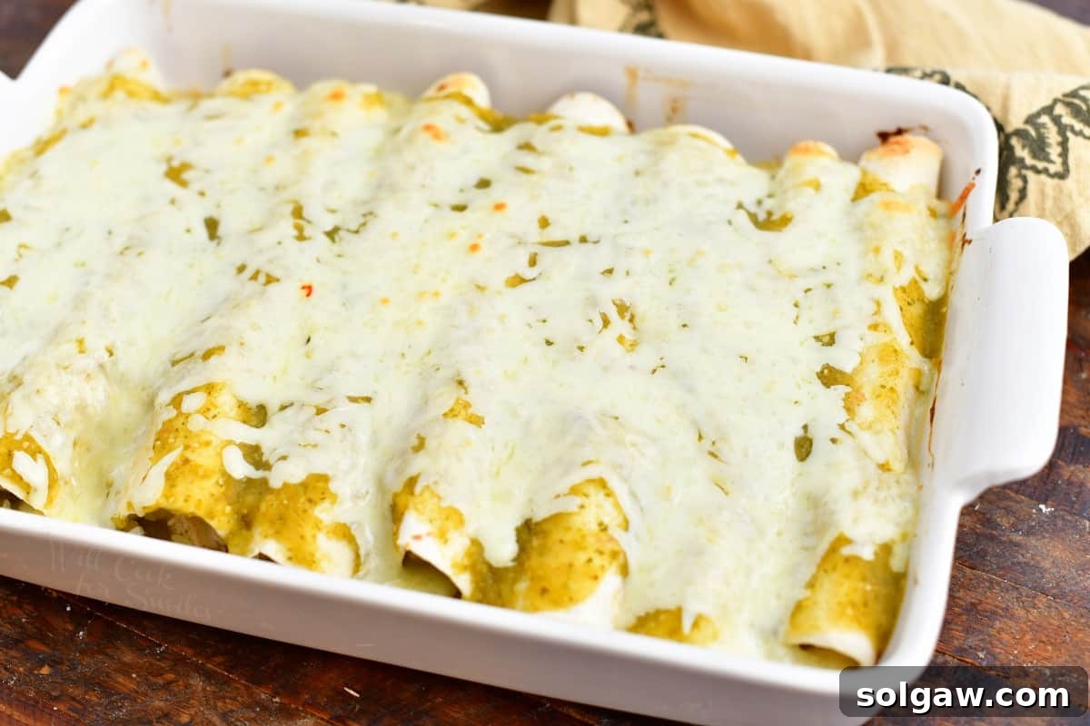 baked chicken enchiladas covered in green sauce and melted cheese in a white casserole dish