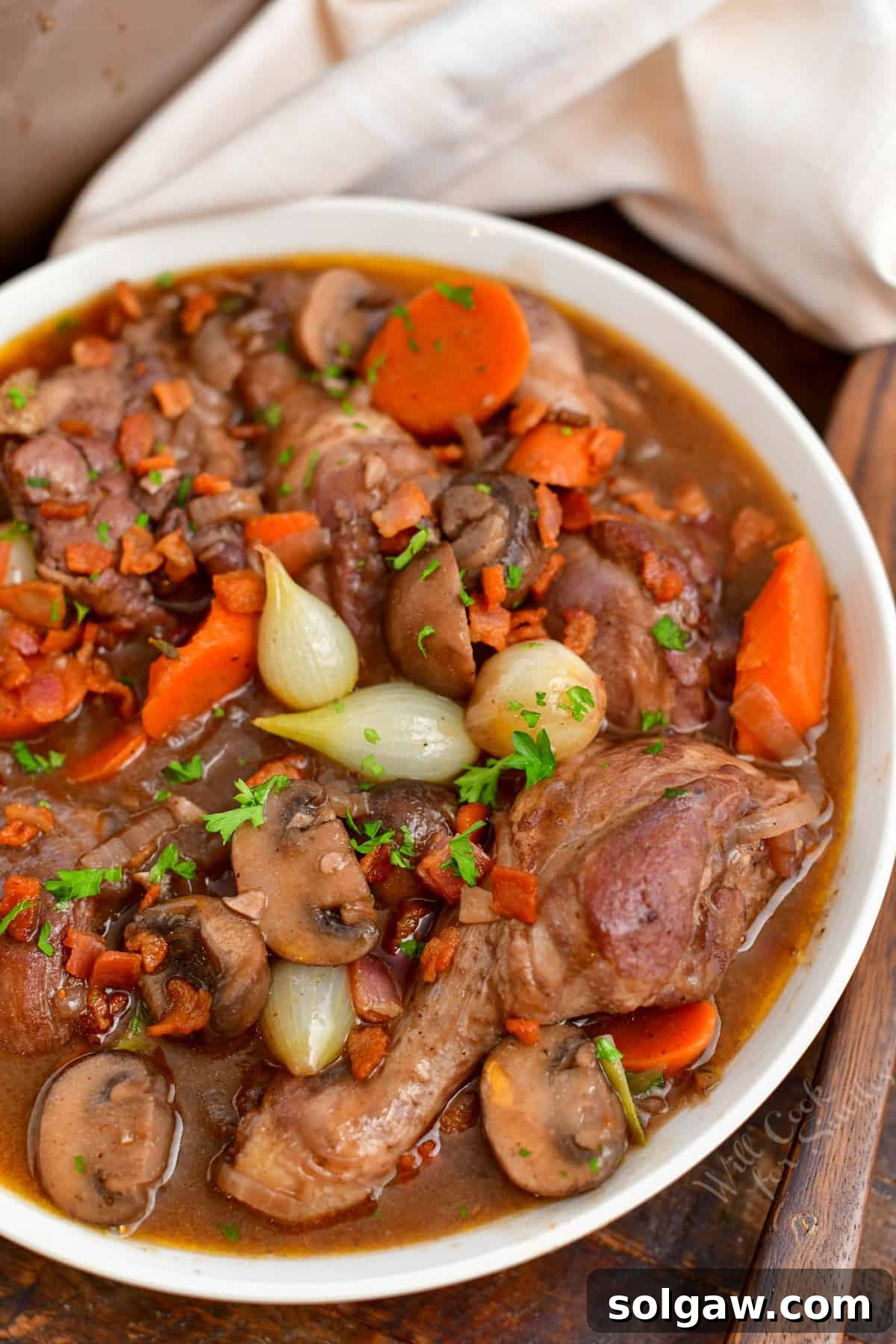 closeup: cooked French chicken recipe in a white bowl with a wooden spoon and cloth napkin